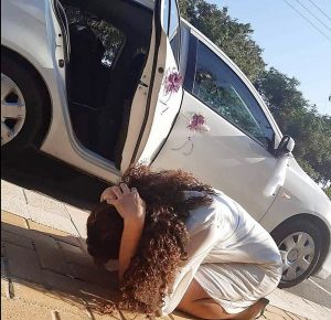 woman crouches next to her car during a rocket attack